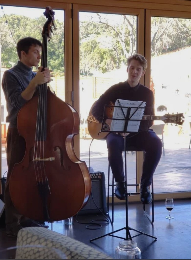 Harley Guio performing live on acoustic guitar with a bassist